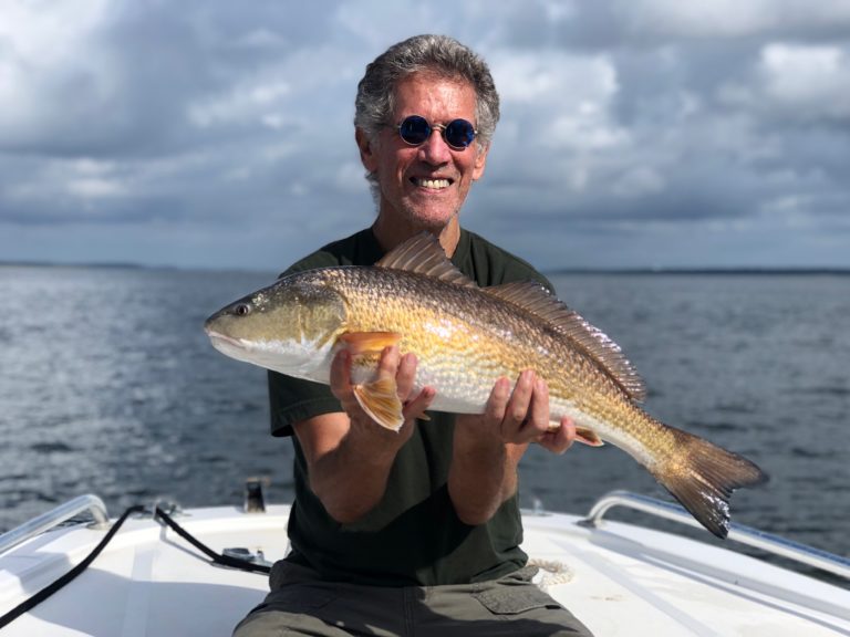 Smiling angler holding a redfish on the bow of the boat