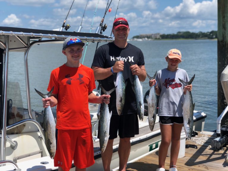 Two kids and an adult holding Spanish mackerel at the dock