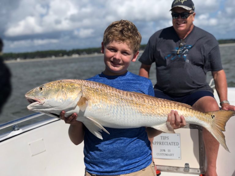 Boy holding a big redfish with an adult angler