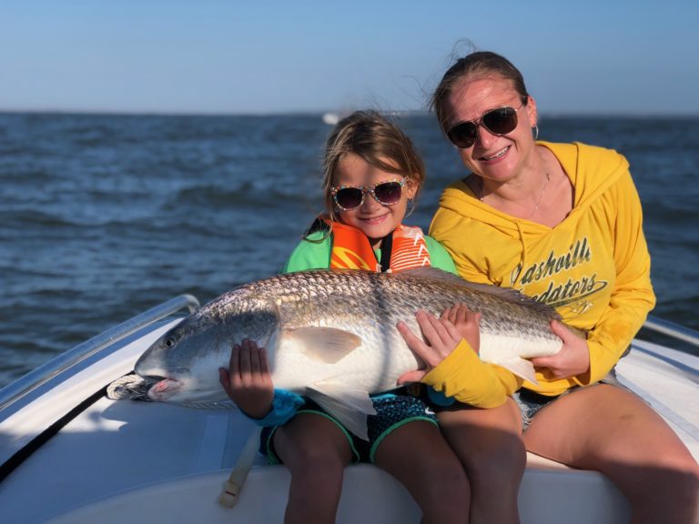 Girl and woman holding a redfish together on the bow